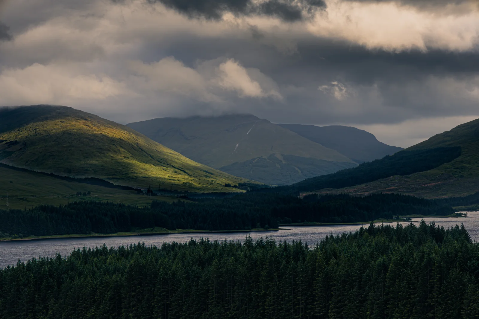 Warm sunlight breaking through clouds above green mountains and a reservoir